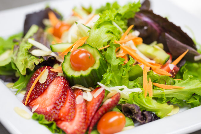 LUC banquet / event catering - decoratively composed fruit and vegetable salad sprinkled with almond slices, featuring cucumber and grape tomato floral decoration off centre.